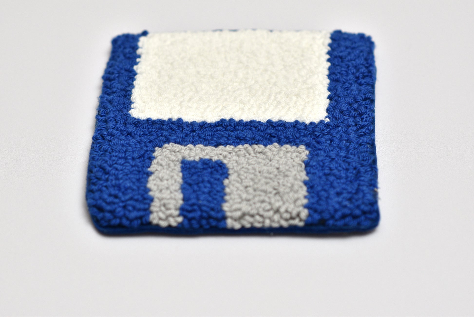 Punch needled coaster shaped like a floppy disk on a white background