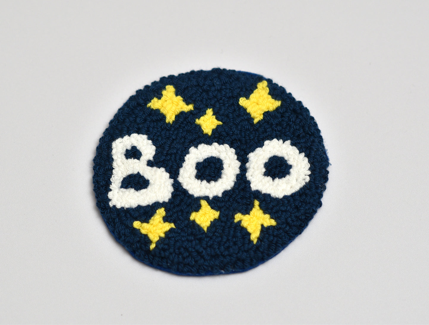 Punch needle coaster with 'BOO' text and yellow stars on a blue background