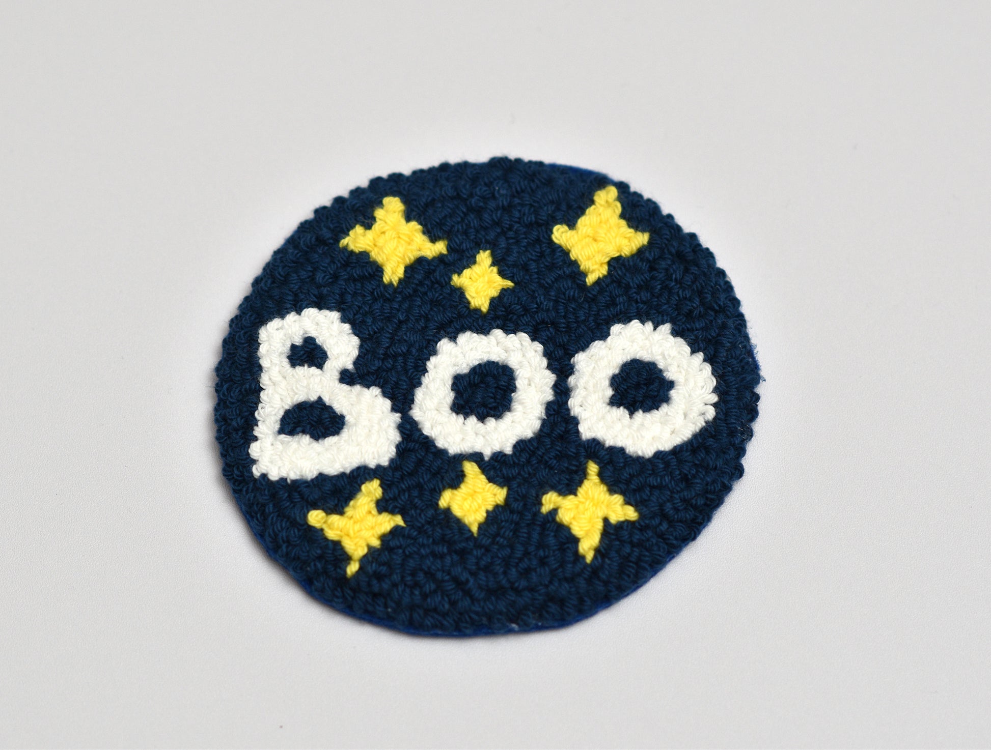 Punch needle coaster with 'BOO' text and yellow stars on a blue background