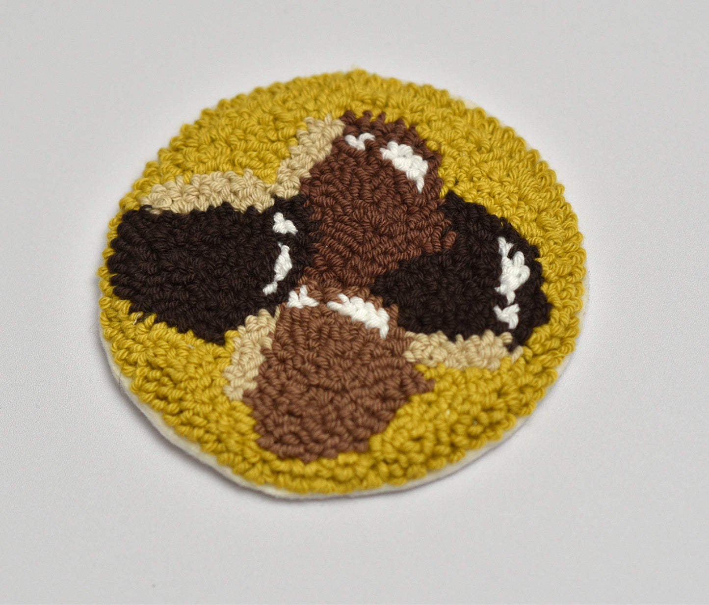 Round punch needle coaster with a chestnuts pattern on a light gray background