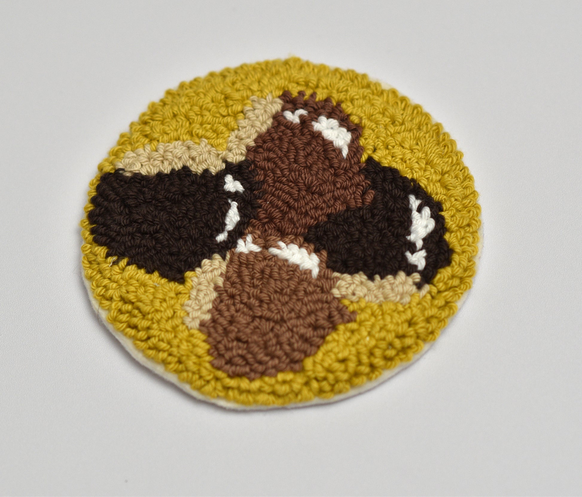Round punch needle coaster with a chestnuts pattern on a light gray background