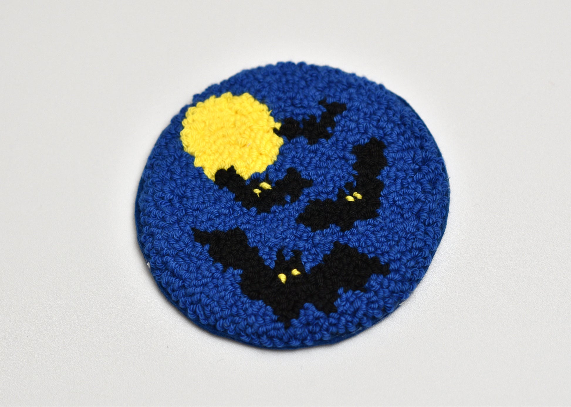 Round blue punch needle coaster with black bats and a yellow moon on a white background