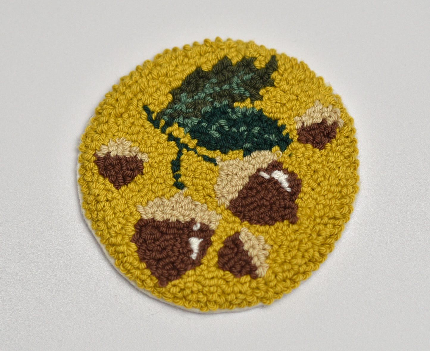Round punch needle coaster with hazelnut acorn design on a yellow background