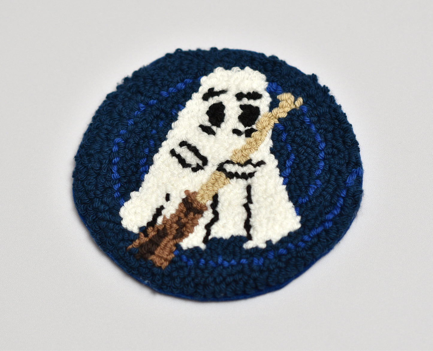 Embroidered coaster of a ghost holding a broom on a blue background