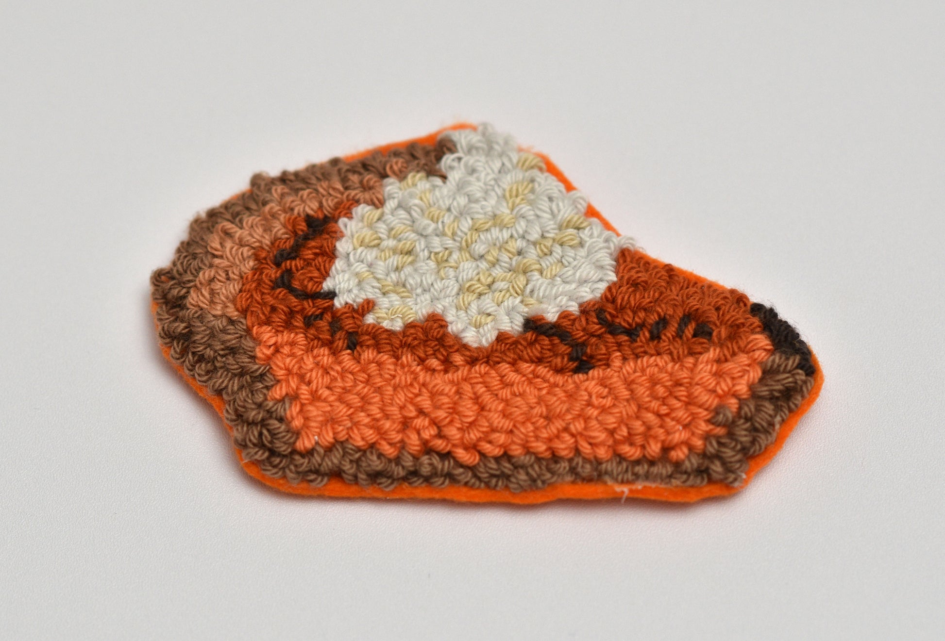 Embroidered pumpkin pie coaster with white filling on a light gray background