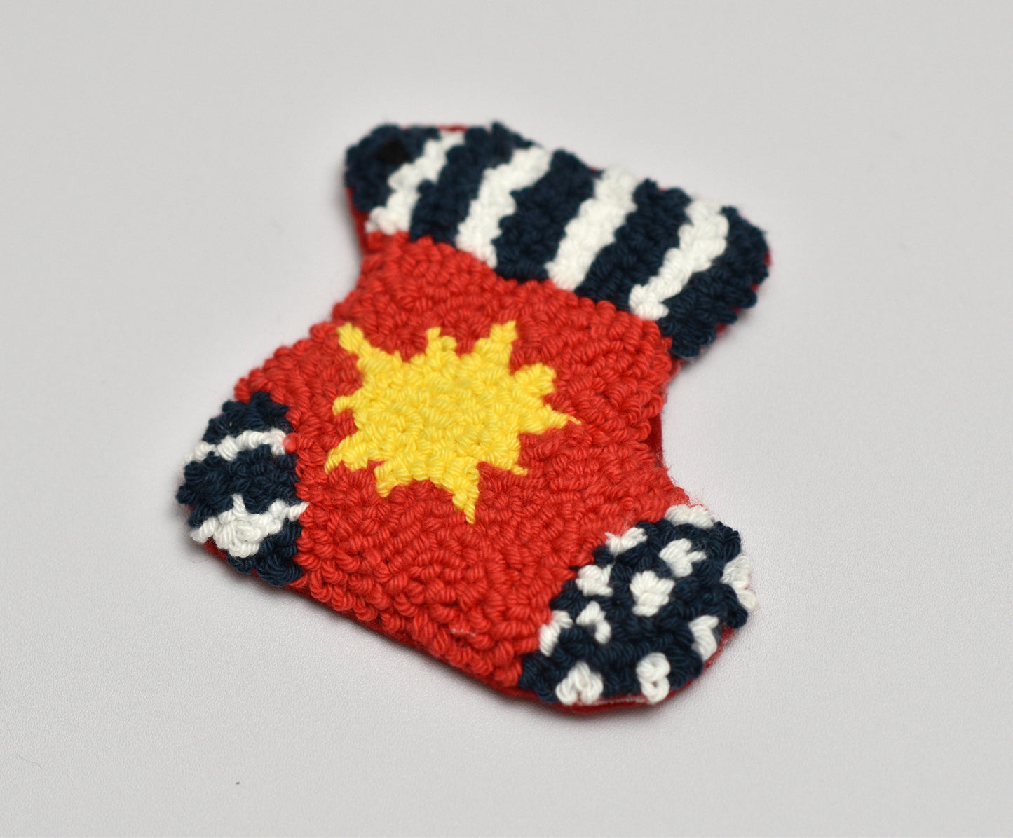 Embroidered punch needle coaster with red center, yellow star, and black and white striped pattern on a gray background