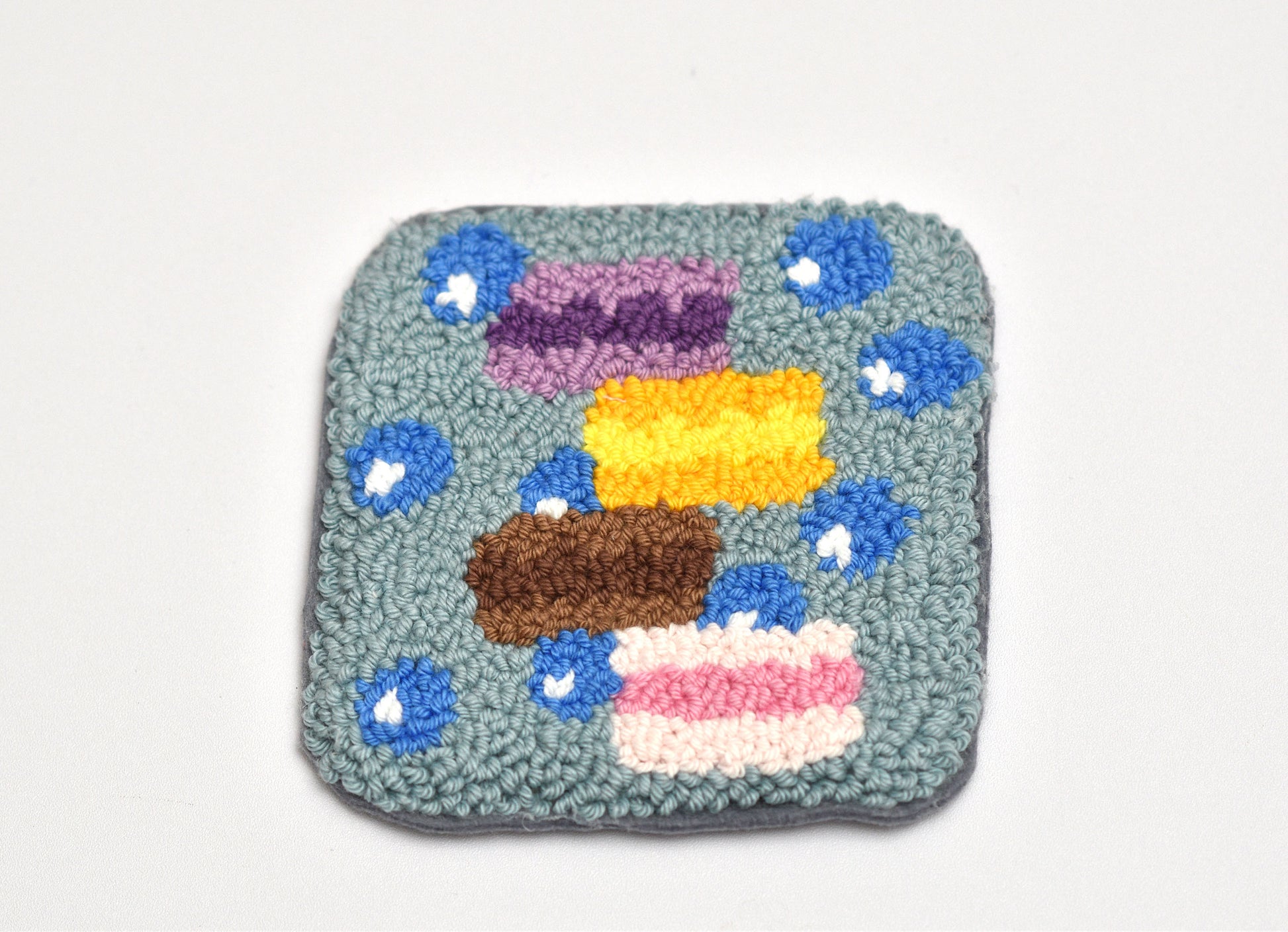 Square textured coaster with colorful macaron design on a white background