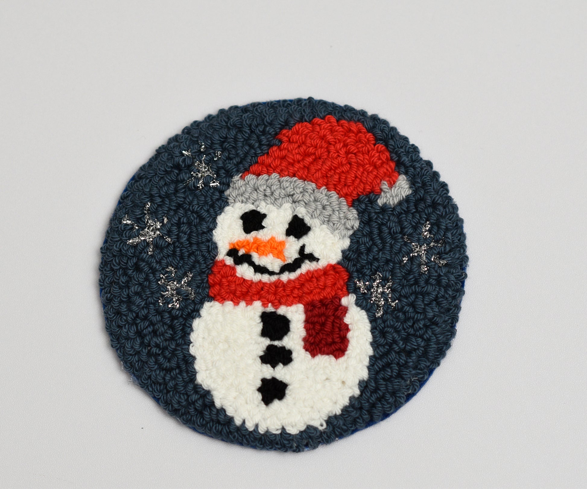 Embroidered snowman coaster with a red hat and scarf on a dark blue background