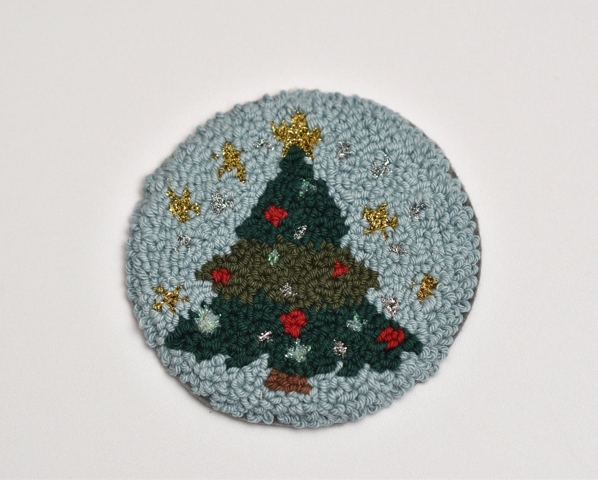 Round punch needle coaster with a Christmas tree design on a light gray background