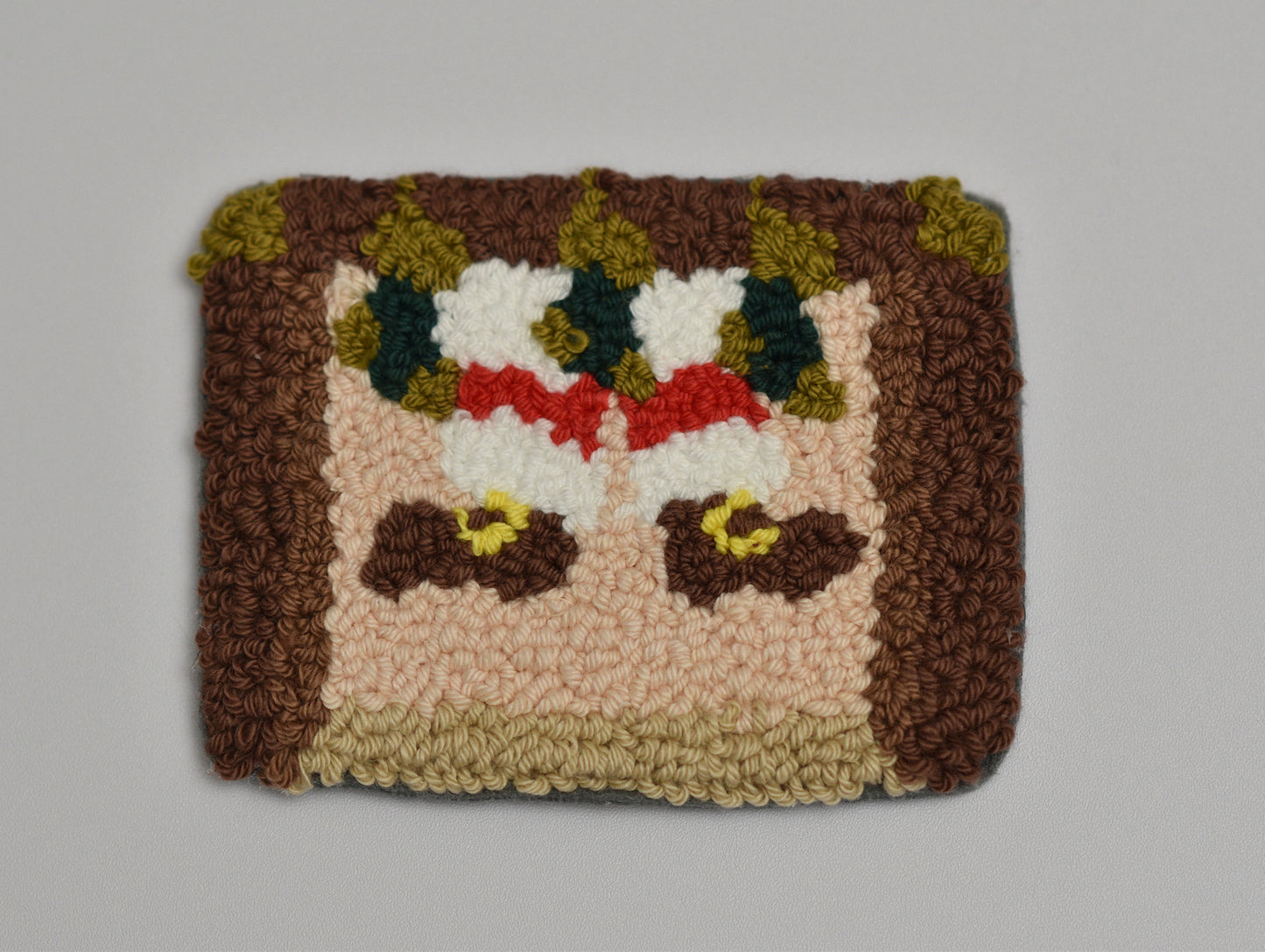 Punch needled coaster with a pattern of Santa stuck in a chimney on a plain background