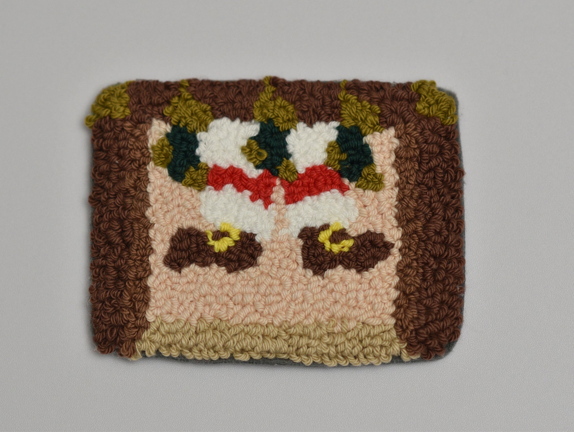 Punch needled coaster with a pattern of Santa stuck in a chimney on a plain background