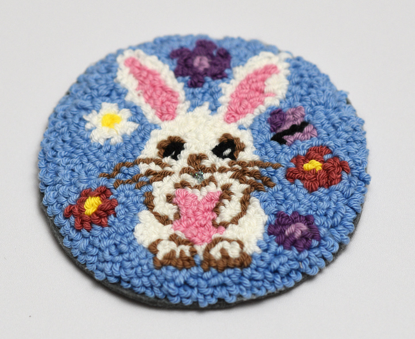 Round embroidered coaster with a bunny and flowers on a blue background