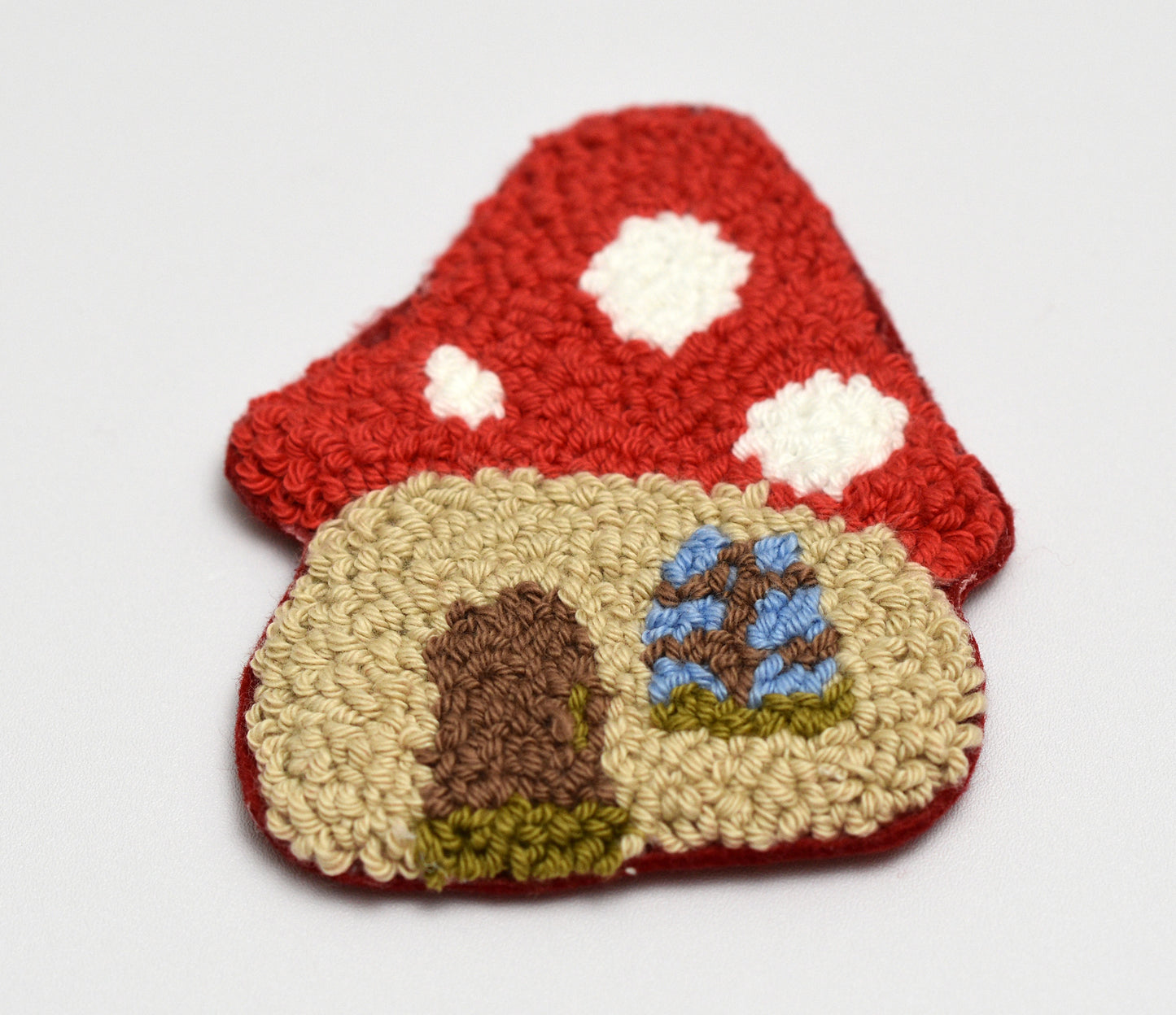 Punch needle coaster with mushroom- shaped house design on a white background