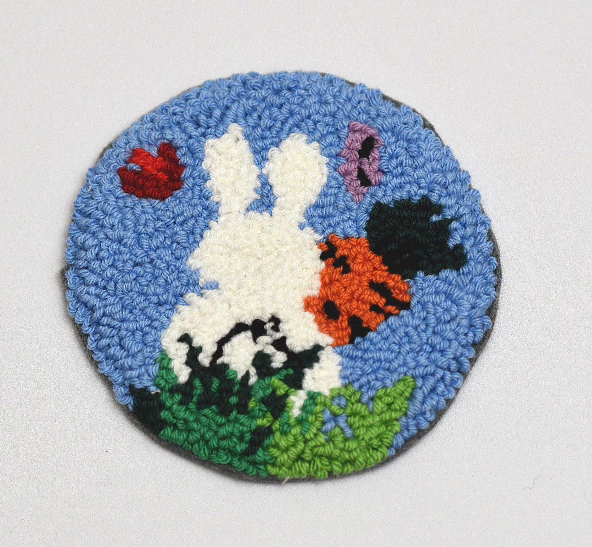 Embroidered coaster with a white Easter rabbit, flowers, and blue background