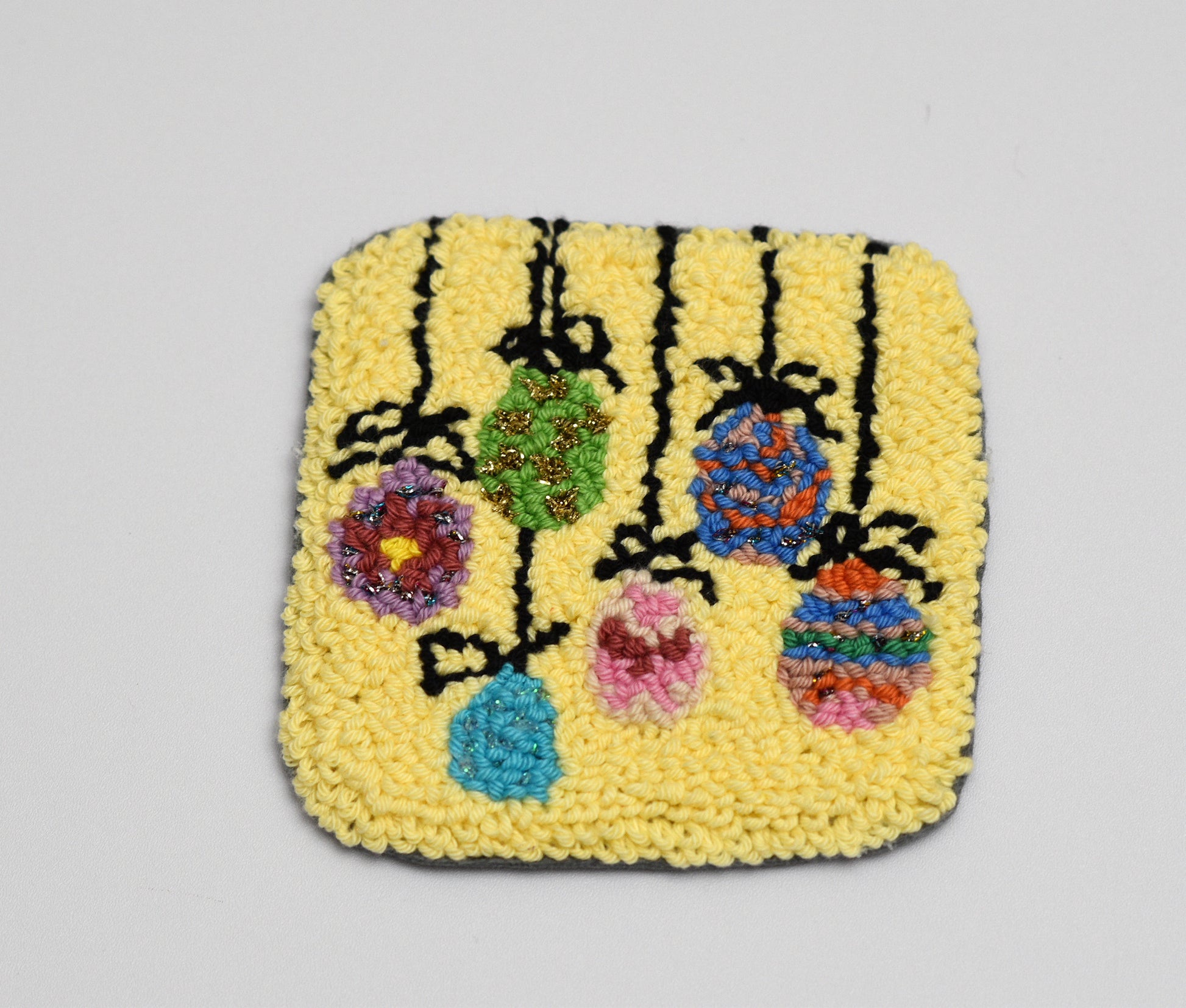 Square woven Easter Egg coaster with floral design on a yellow background