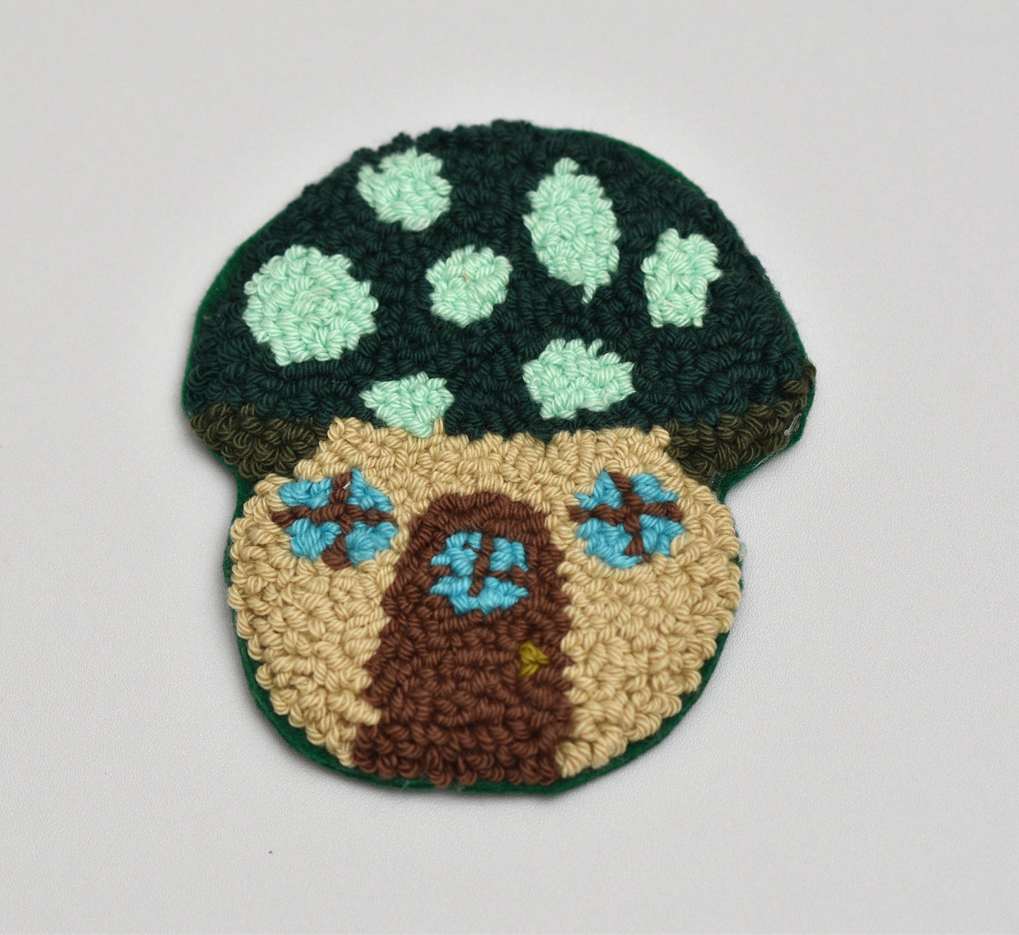 Punch needled mushroom coaster with a door and flowers on a light gray background