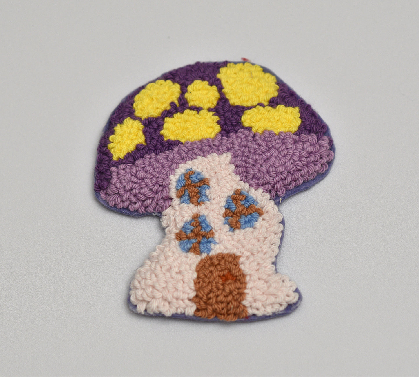Decorative punch needle coaster with a mushroom design on a gray background