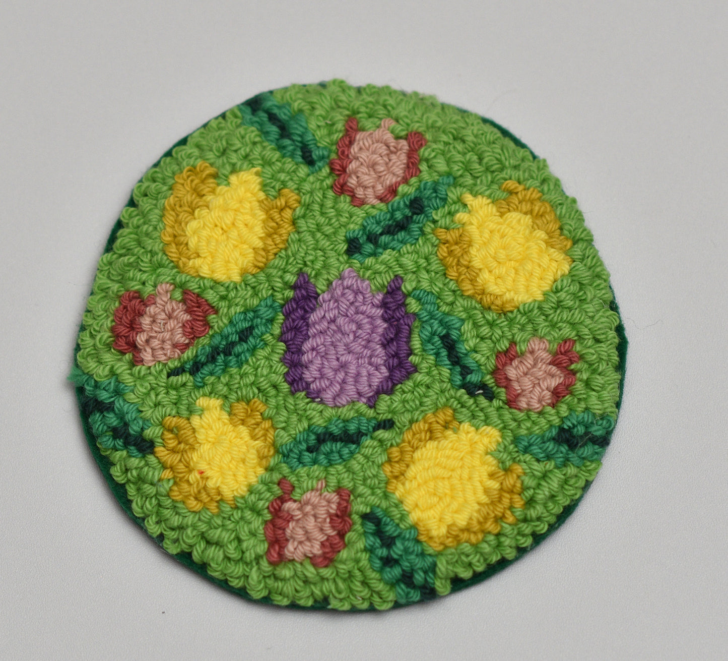 Round green rug with floral tulip patterns on a gray background
