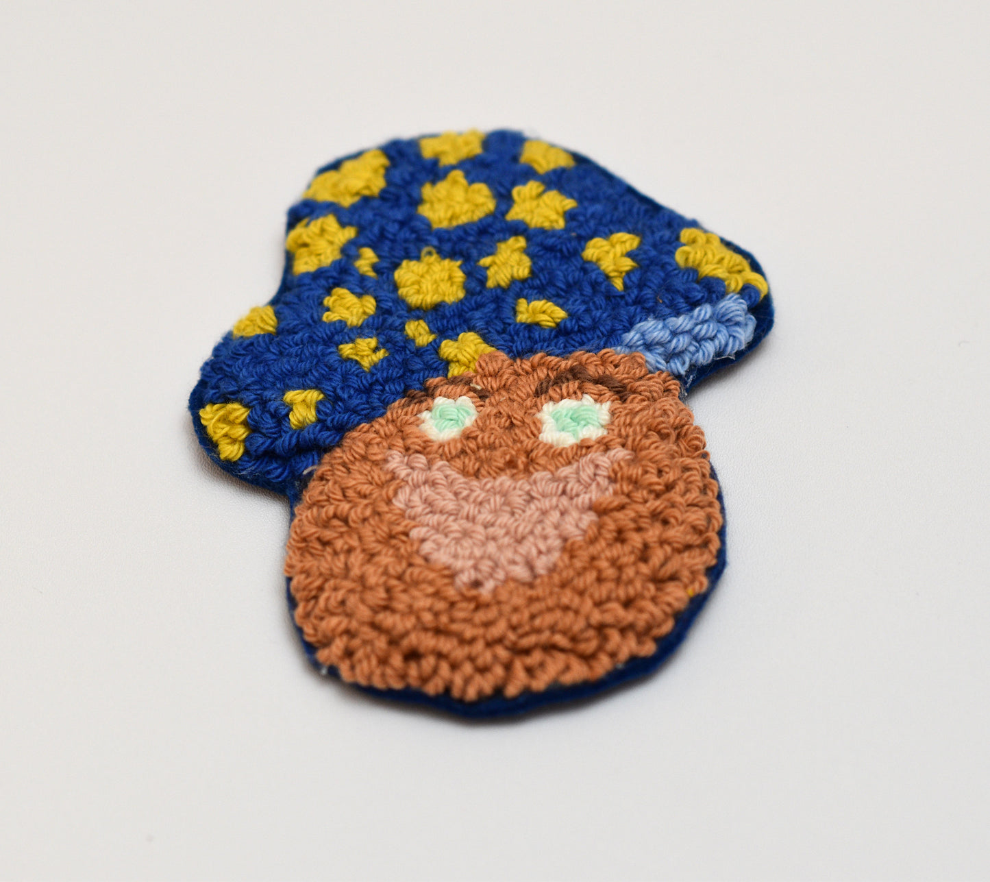 Punch needled mushroom shaped coaster with blue hat and yellow dots on a light gray background