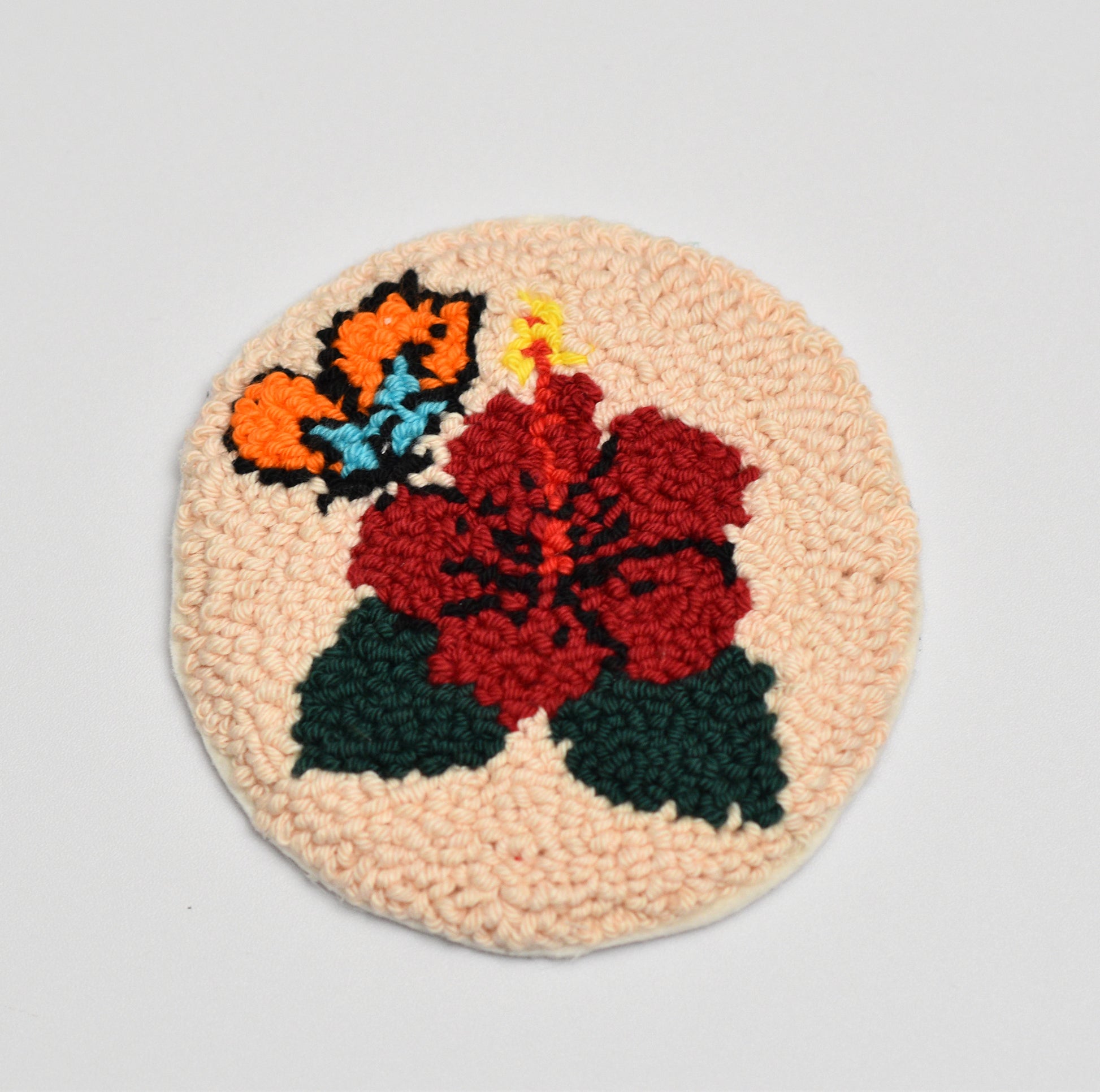 Round woven coaster with floral hibiscus design on a light gray background