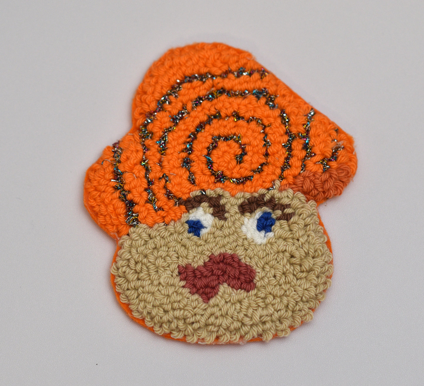 Punch needle coaster with mushroom character with orange hair and a neutral expression on a gray background
