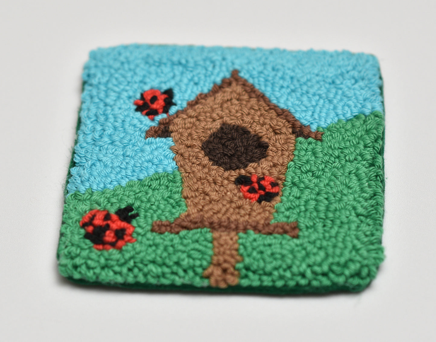 Handmade rug with a birdhouse and ladybugs design on a blue and green background