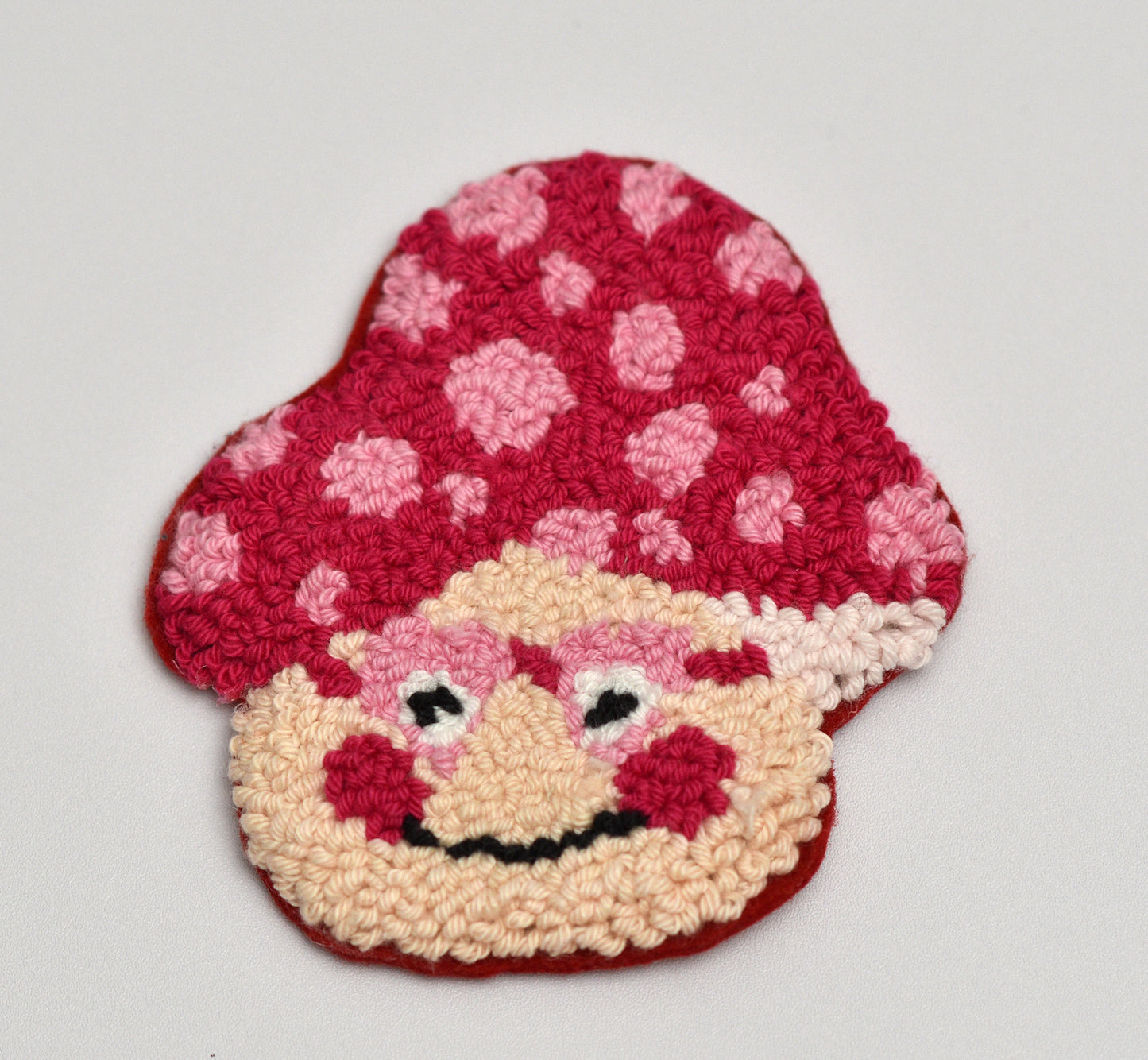 Handmade coaster with a mushroom character with a red hat and pink dots on a light gray background