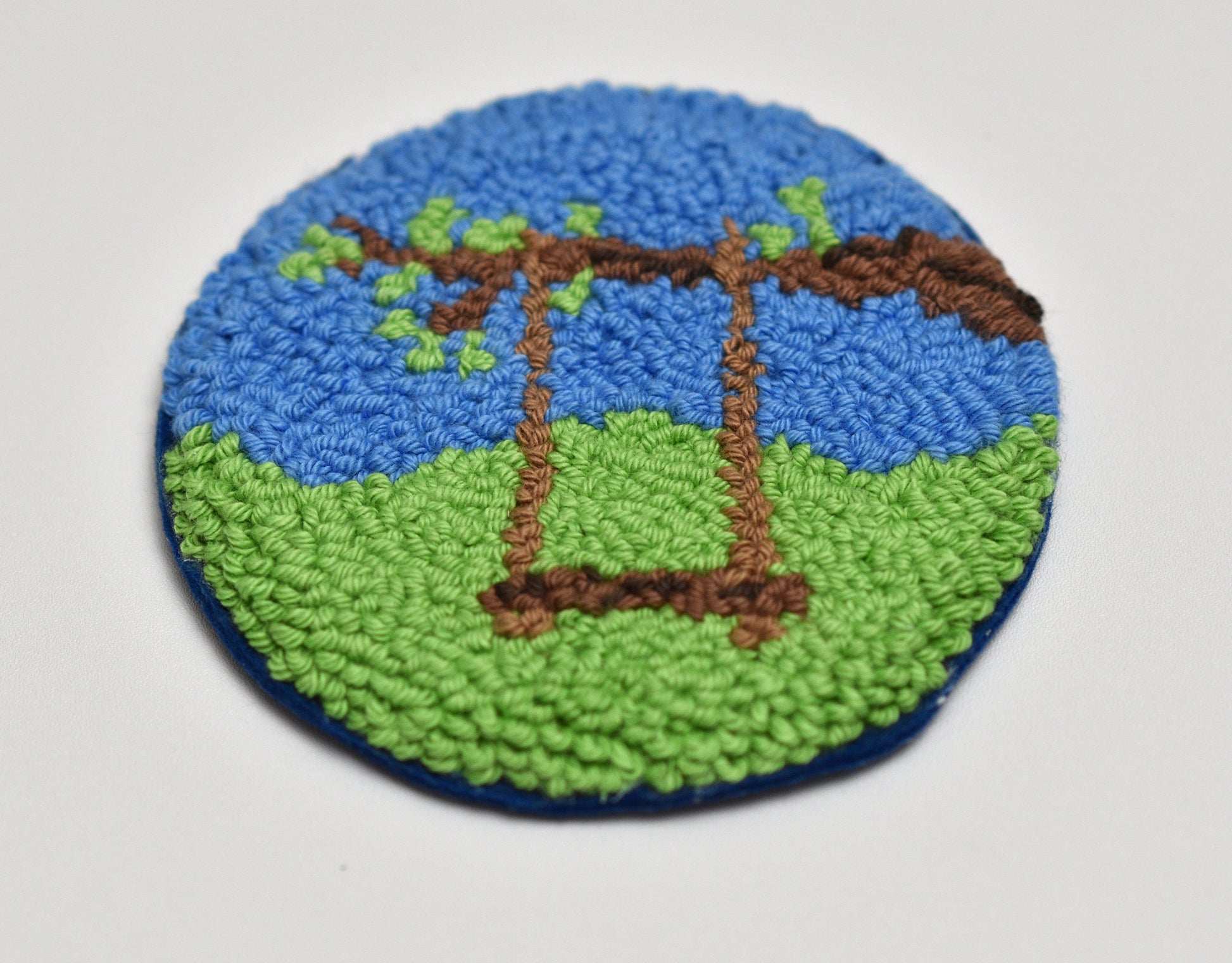 Round embroidered mug rug with a swing set design on a blue and green background