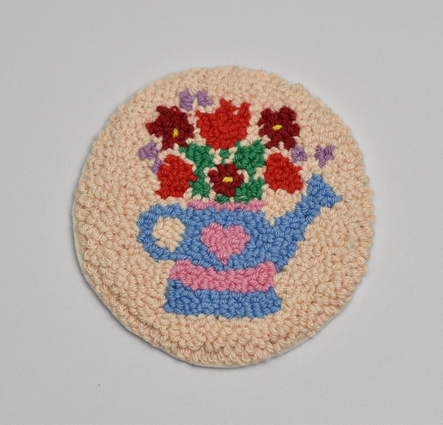 Round woven coaster with a blue watering can and inside red flowers on a beige background