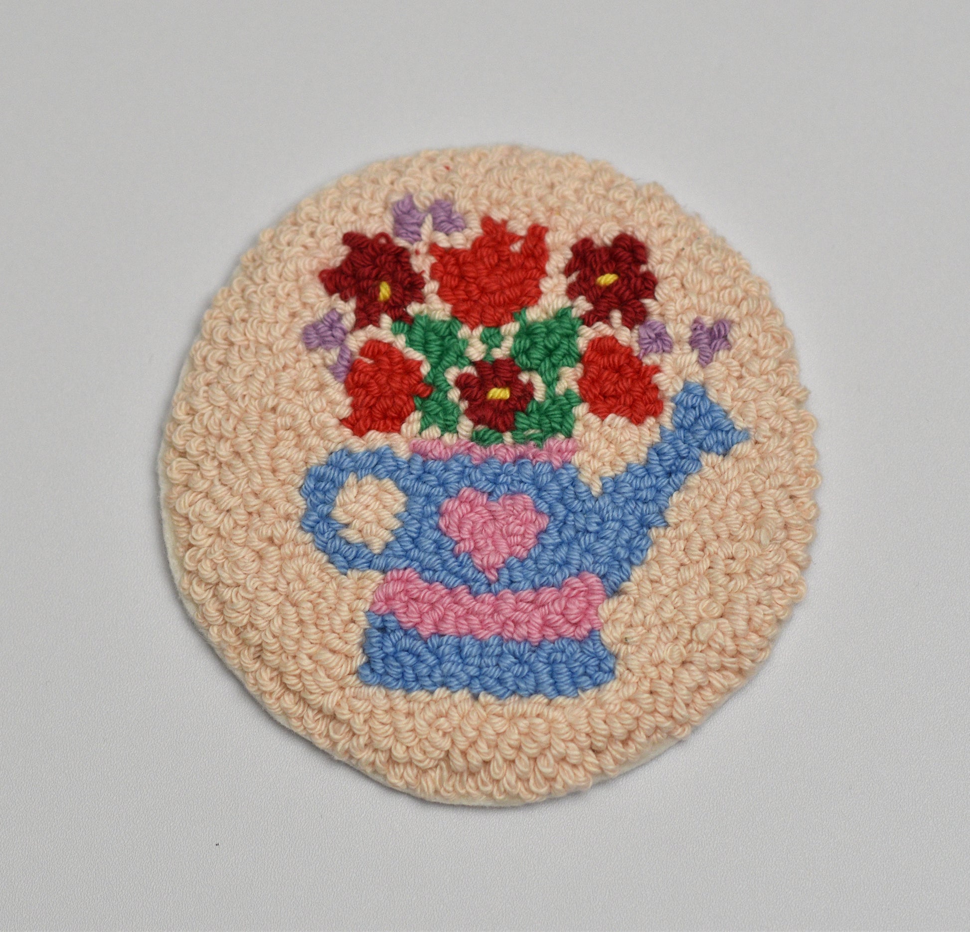Round woven coaster with a blue watering can and inside red flowers on a beige background