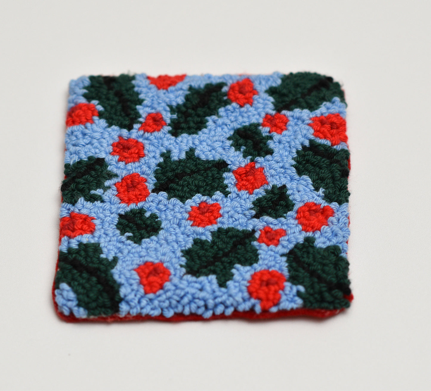 Embroidered  square coaster with red and green mistletoe pattern on a light gray background