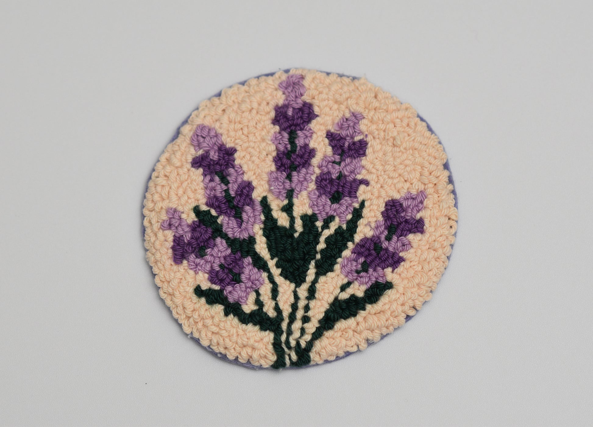 Round punch needled coaster with lavender design on a gray background