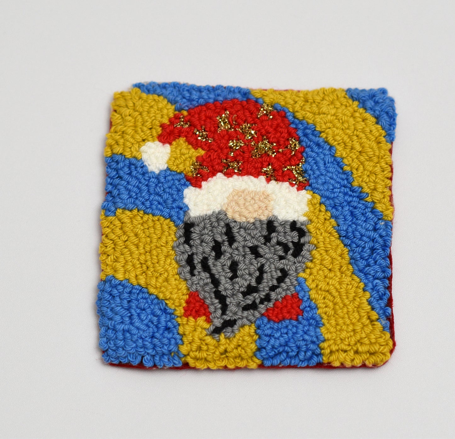 Square coaster with a embroidered design of a gnome on a gray background