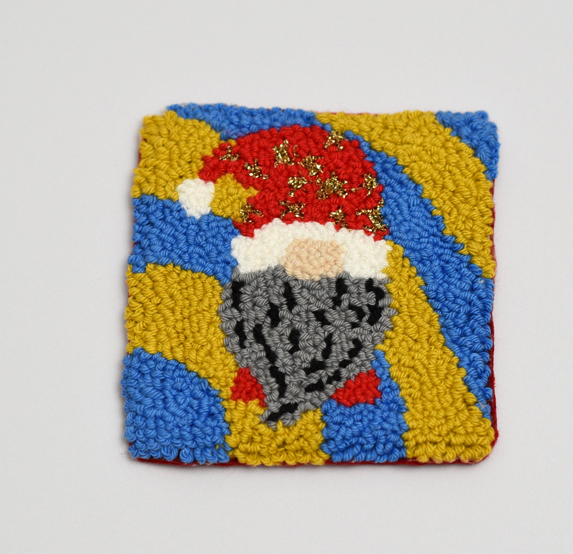 Square coaster with a embroidered design of a gnome on a gray background