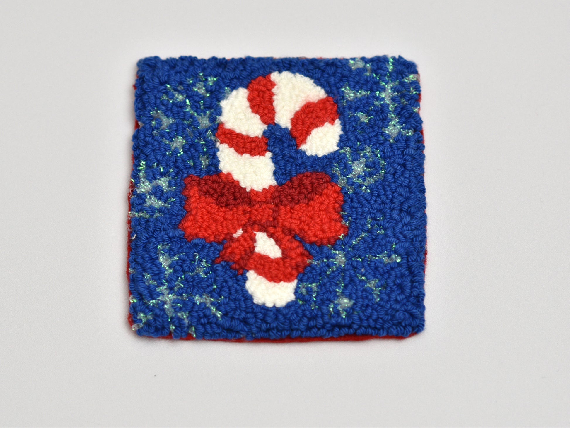 Square punch needle coaster with a candy cane design on a blue background