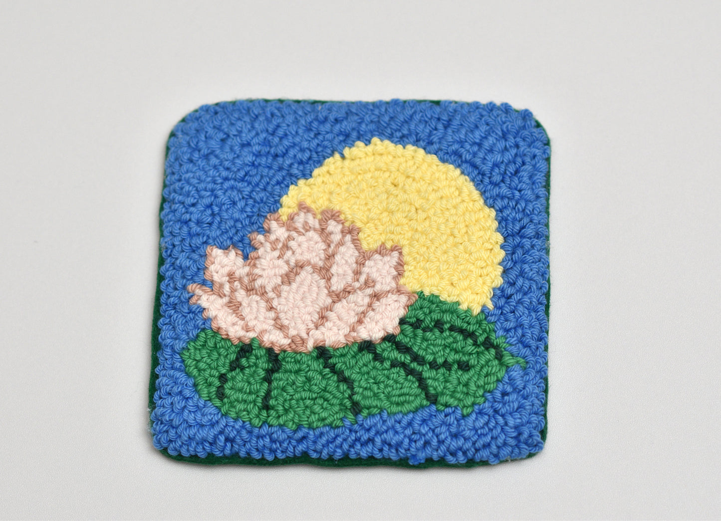 Square woven coaster with a water lily design on a light gray background