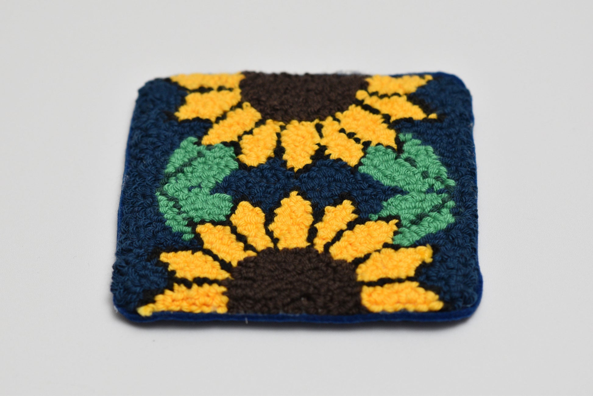 Square woven mug rug with sunflower design on a gray background