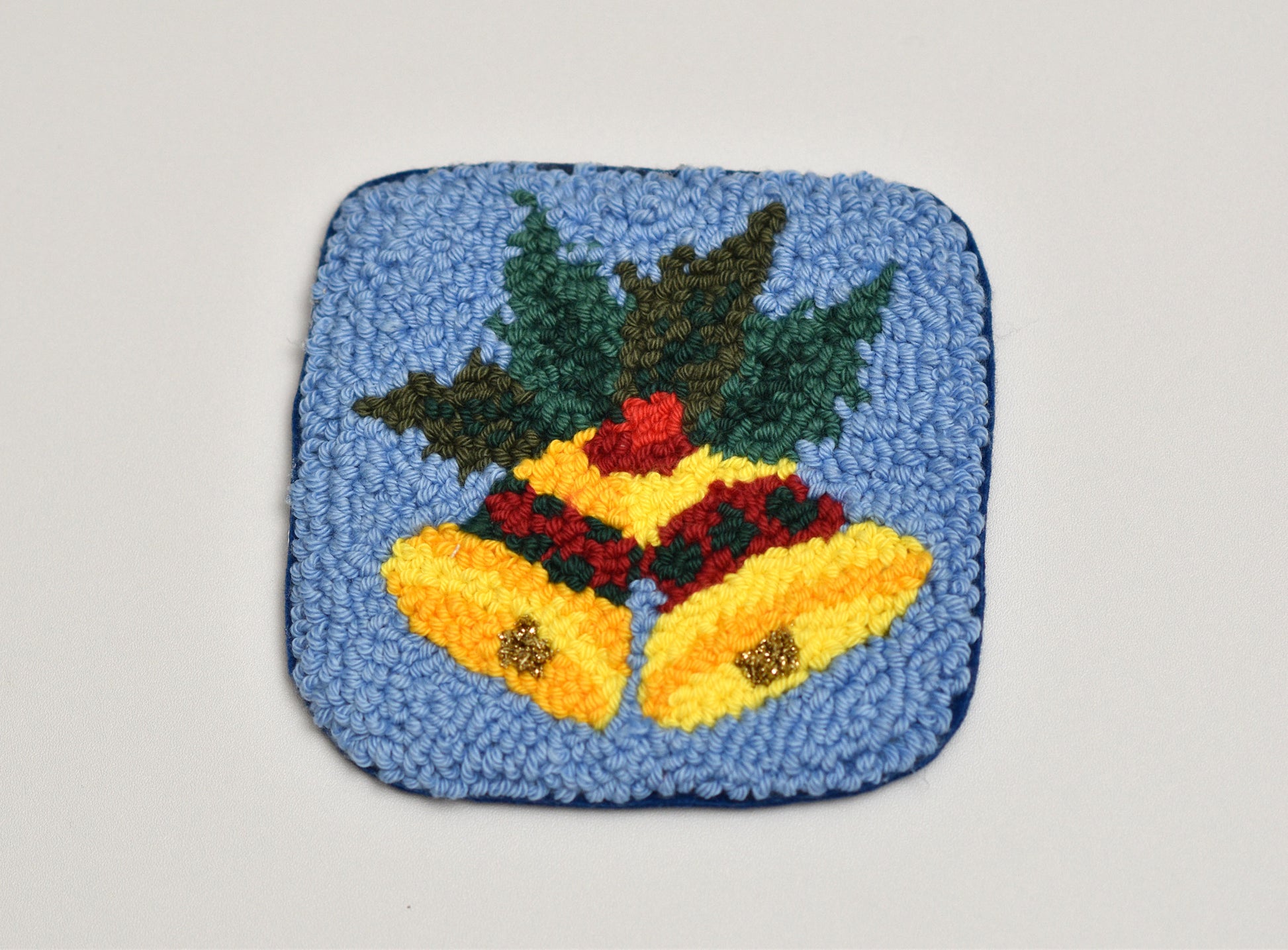 Decorative punch needle mug rug with yellow bells and greenery on a blue background