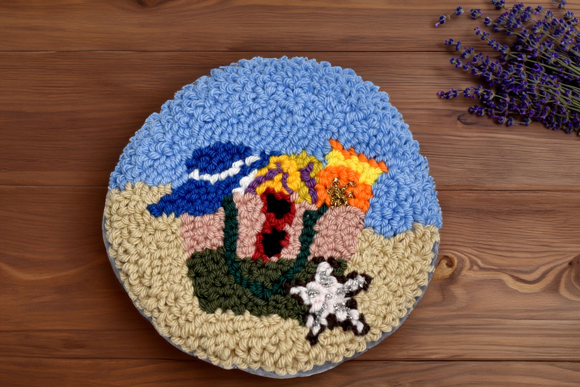 Round punch needle coaster with colorful floral design on a wooden surface