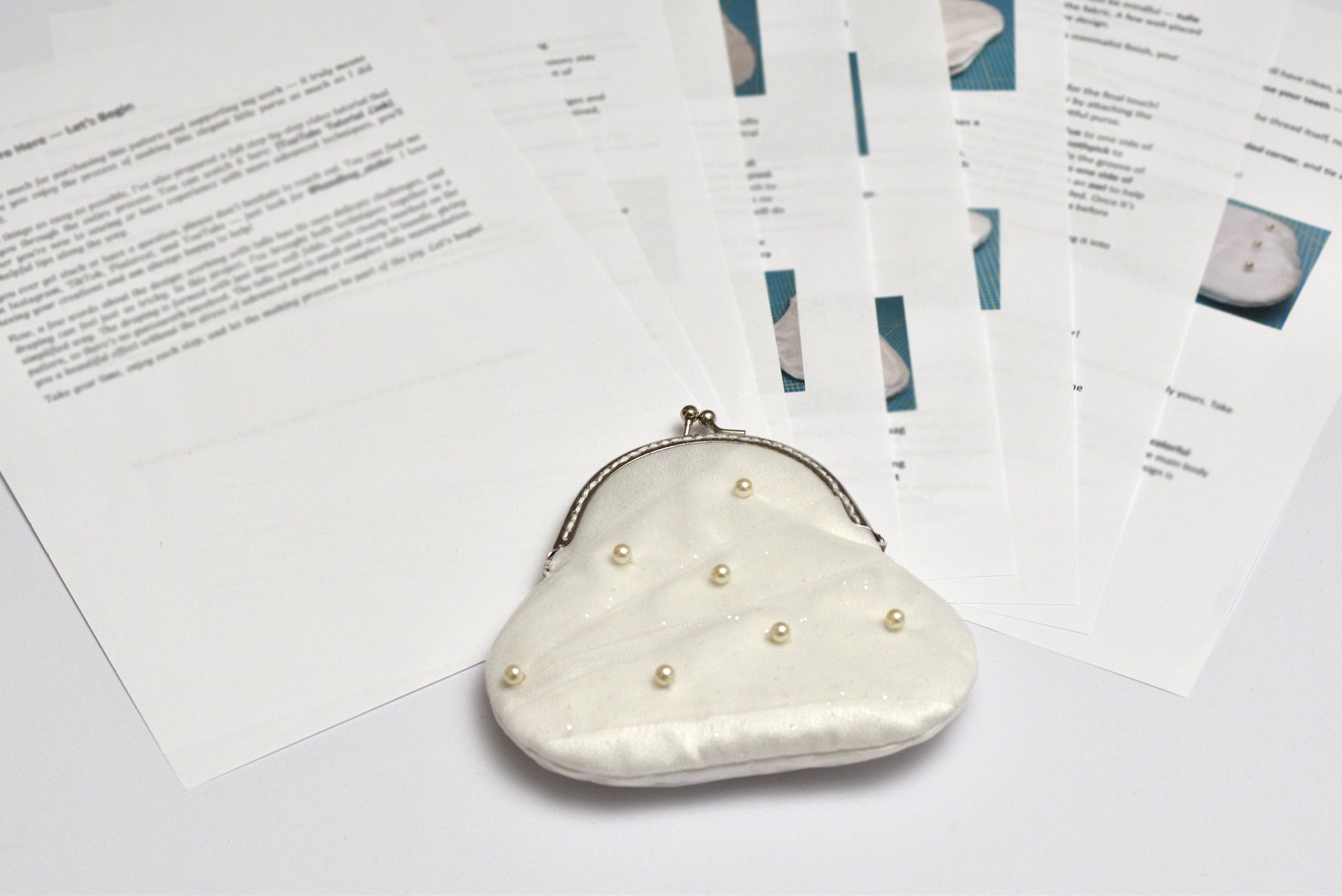 White pearl-handled clutch bag on a white surface with printed how to do pages in the background