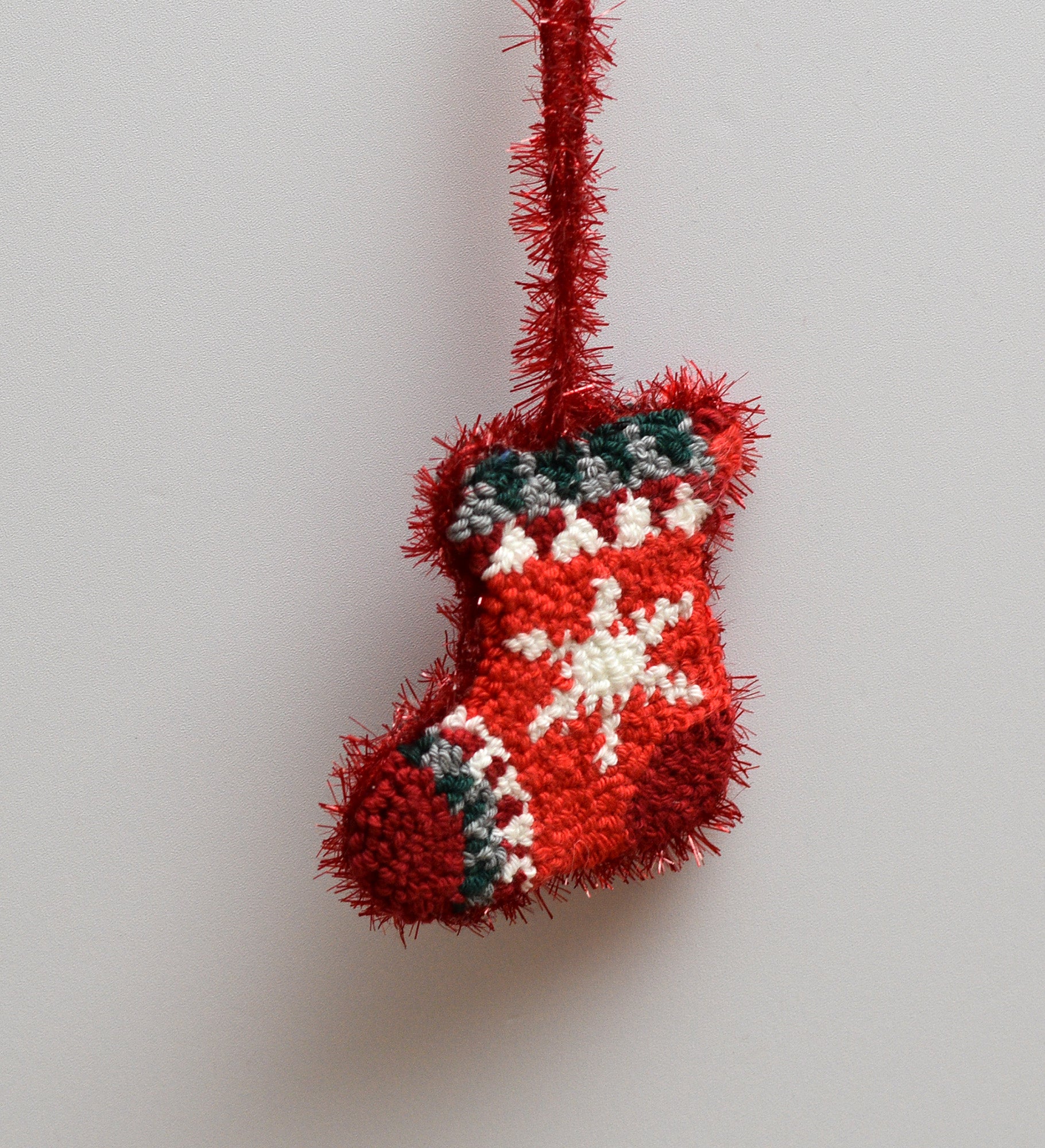 Red punch needled Christmas stocking with a snowflake design on a light gray background