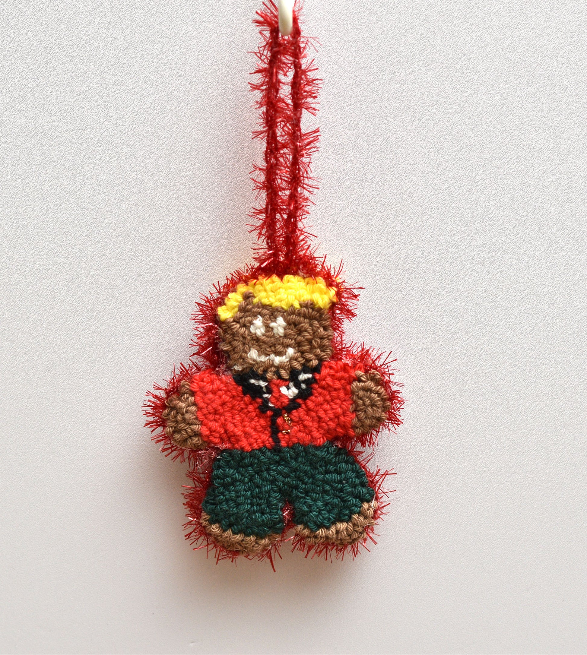 Punch needled gingerbread man ornament with red jacket and yellow hat on a white background