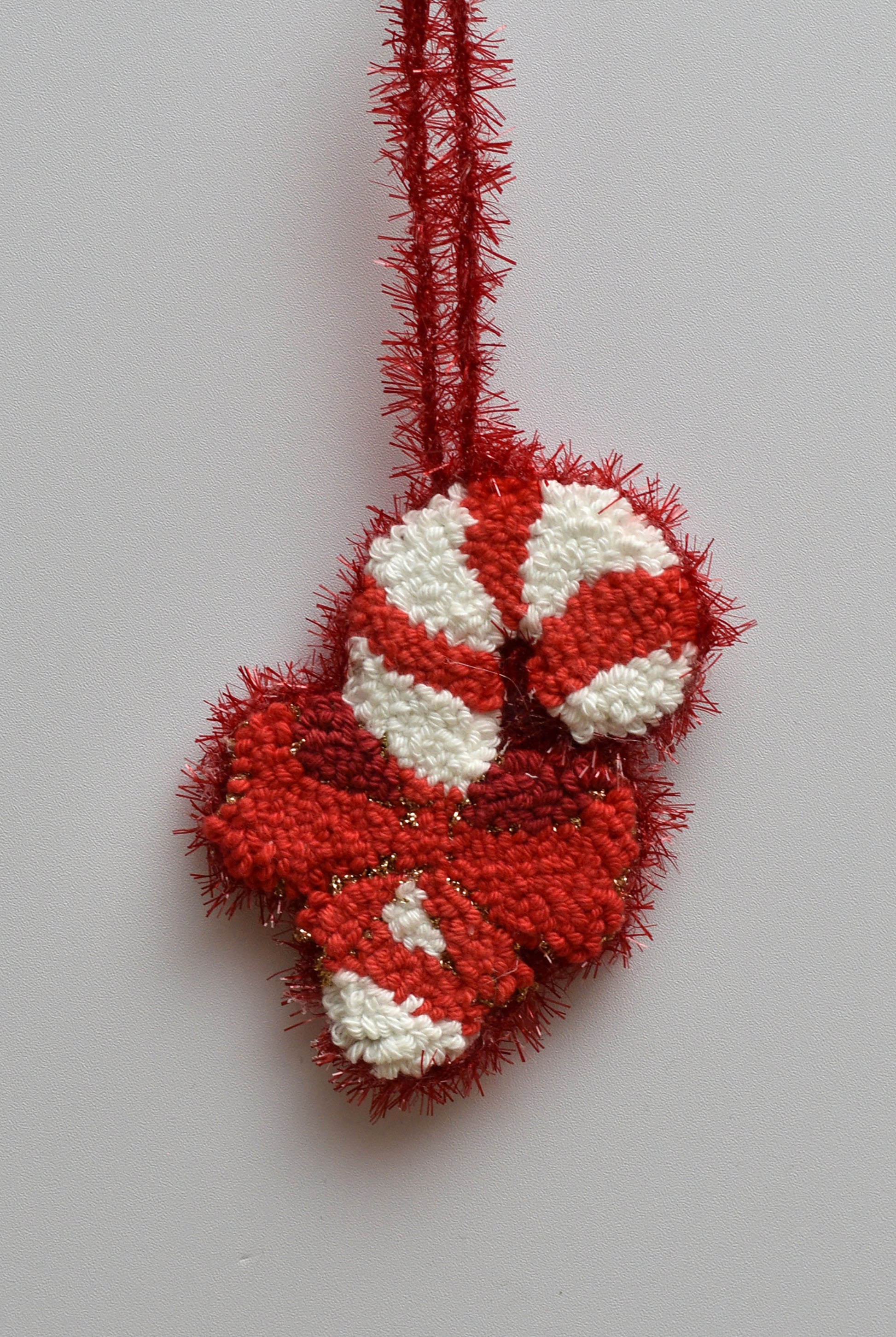 Red and white punch needled candy cane ornament on a light gray background