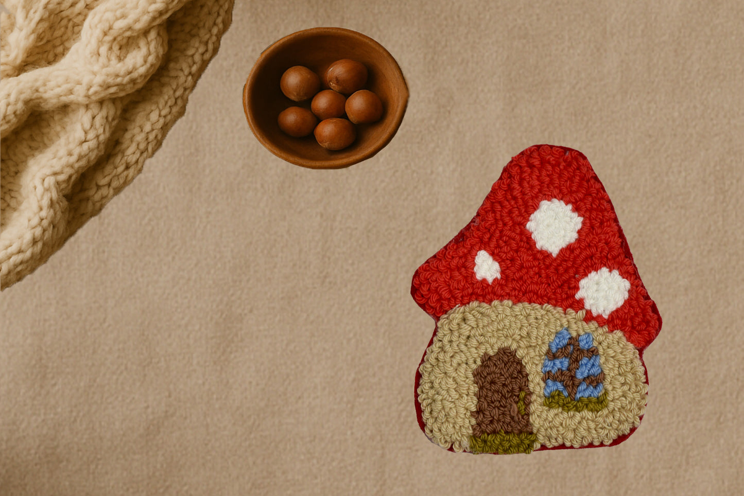 Textured surface with a red mushroom-shaped mug rug, wooden bowl with nuts, and textured fabric.