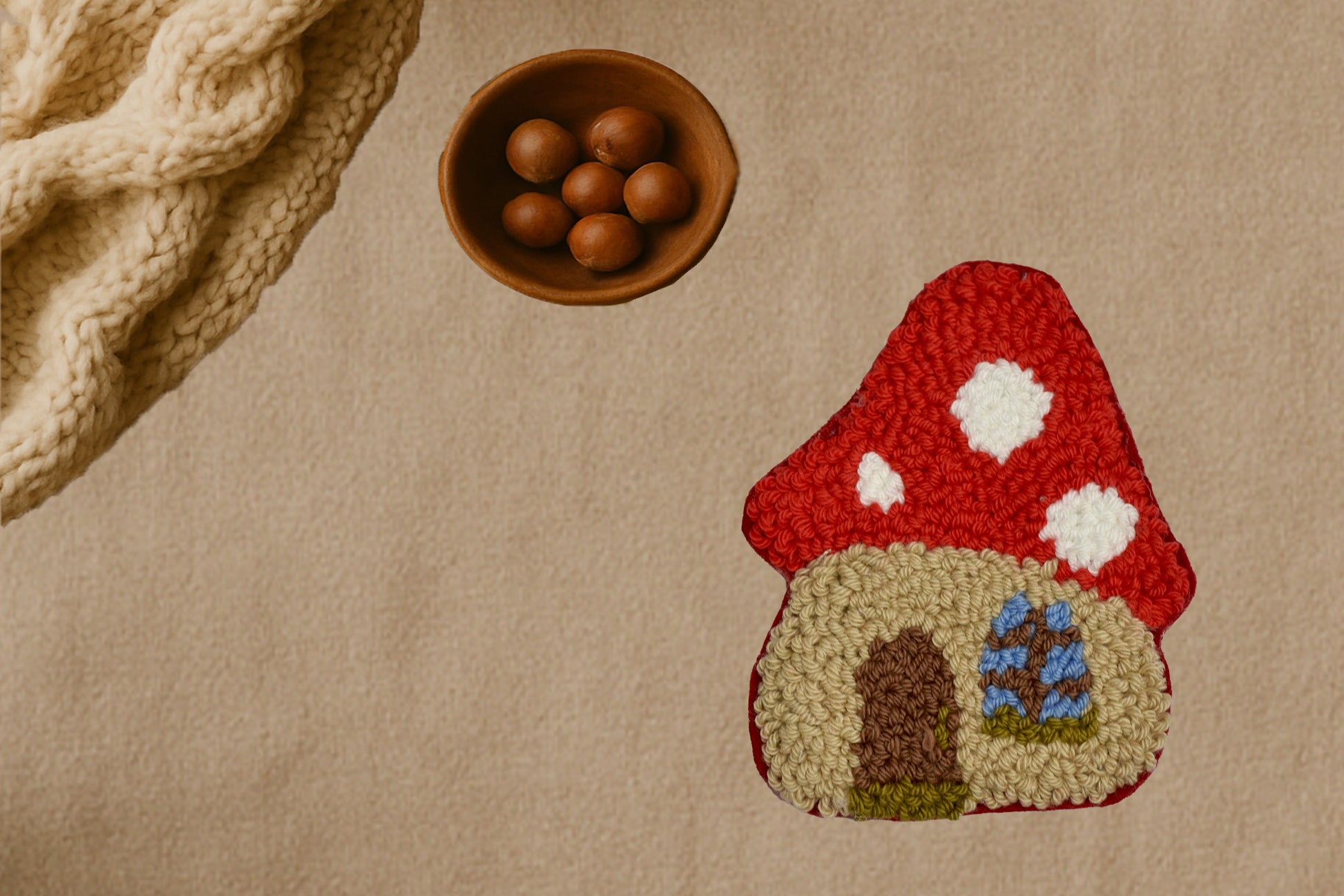Textured surface with a red mushroom-shaped mug rug, wooden bowl with nuts, and textured fabric.