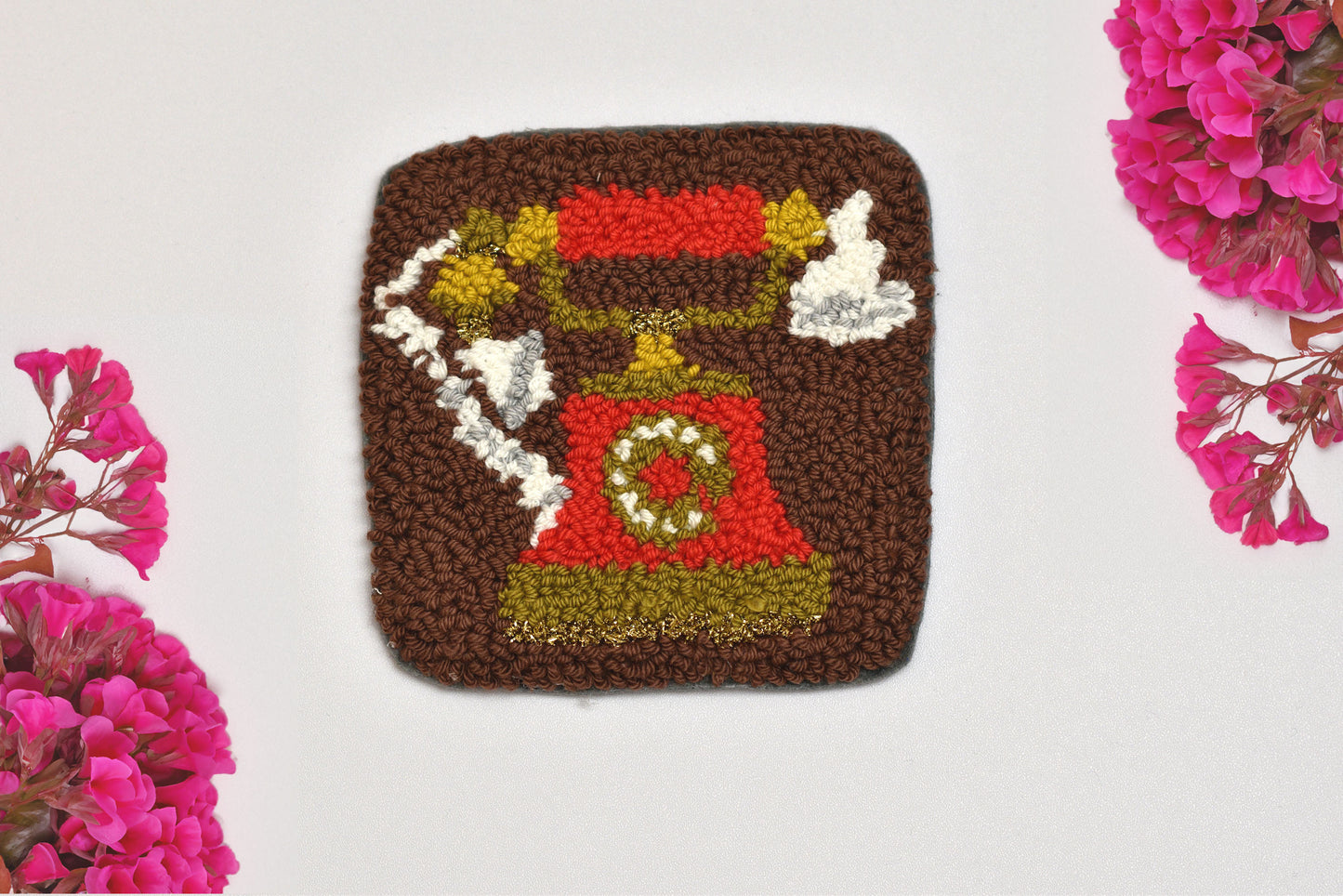 Punch needled square coaster with a telephone design on a white background with pink flowers.