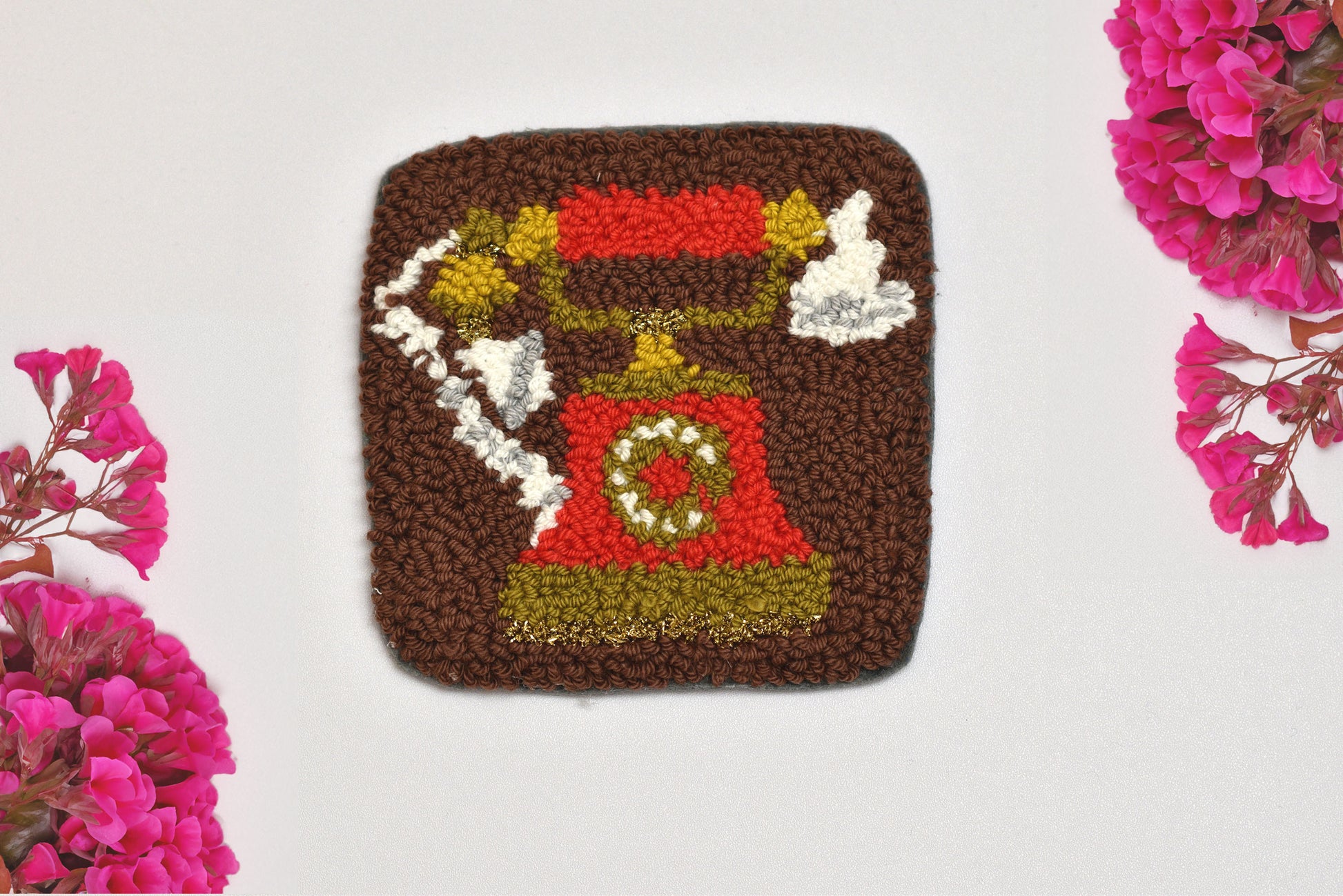 Punch needled square coaster with a telephone design on a white background with pink flowers.