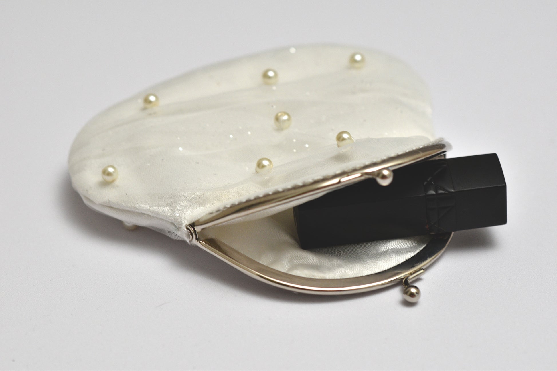 White clutch purse with pearl embellishments on a light gray background