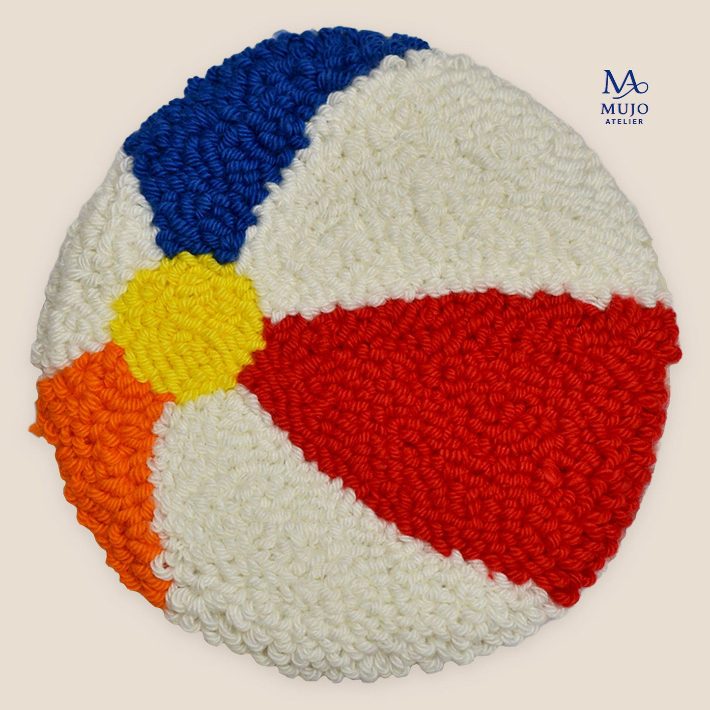 Colorful beach ball punch needle coaster with red, blue, yellow, orange and cream yarn, shown on a neutral cream background with Mujo Atelier logo.