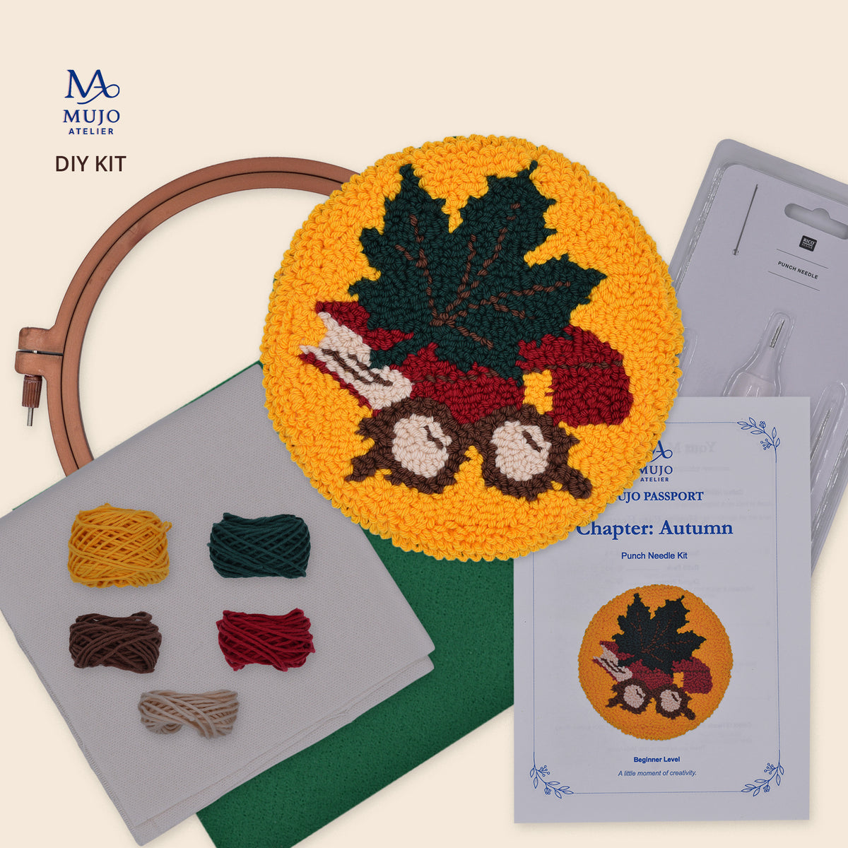 Muijo Atelier DIY Kit for Chapter Autumn, featuring a completed circular punch needle coaster design with a maple leaf and eye glasses, a wooden hoop, yarn balls, a pattern passport, and a punch needle on a light beige background.